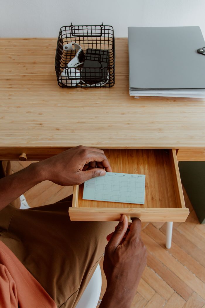Persons hands organizing a desk drawer with stationery, showcasing a tidy workspace.